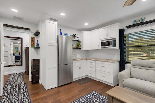 kitchen with appliances with stainless steel finishes, dark hardwood / wood-style floors, light stone countertops, and white cabinets