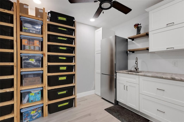 kitchen featuring stainless steel refrigerator, sink, white cabinets, ceiling fan, and light hardwood / wood-style flooring