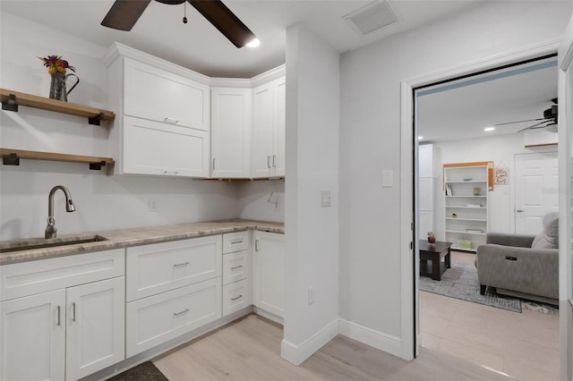 kitchen with sink, ceiling fan, light stone counters, light hardwood / wood-style floors, and white cabinets