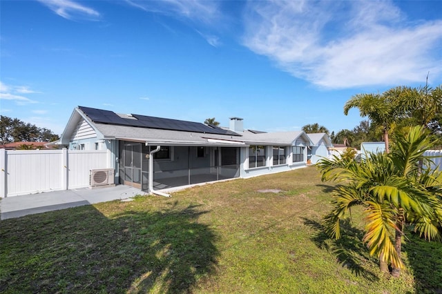 rear view of property featuring a lawn, ac unit, a sunroom, and solar panels