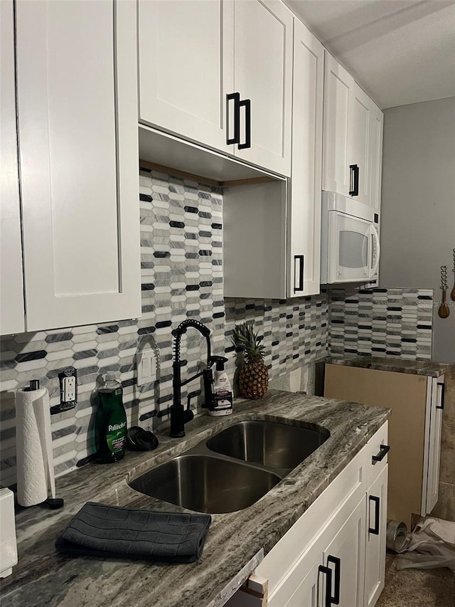 kitchen with white cabinetry, backsplash, sink, and stone counters