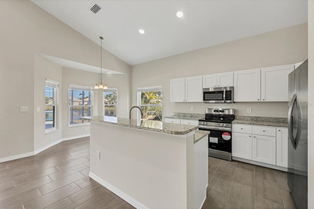 kitchen with appliances with stainless steel finishes, an island with sink, pendant lighting, light stone countertops, and white cabinets