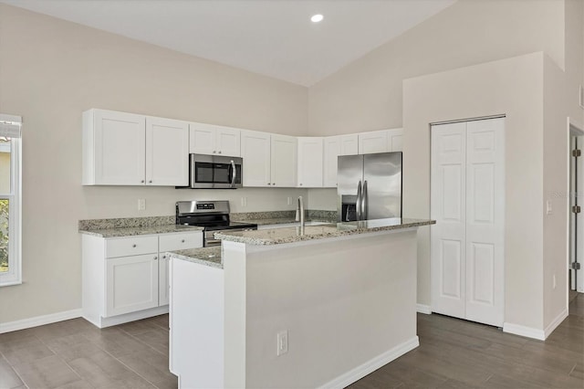 kitchen featuring a kitchen island with sink, light stone countertops, stainless steel appliances, and white cabinets