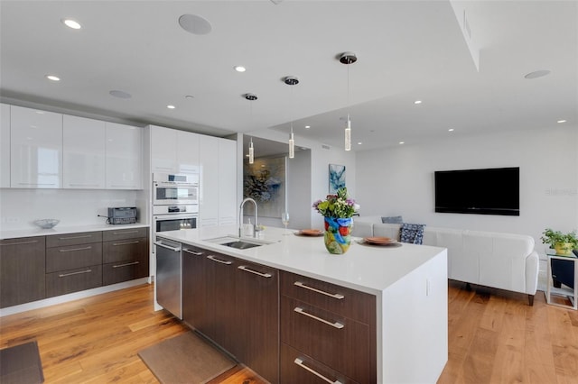 kitchen featuring sink, white double oven, a kitchen island with sink, hanging light fixtures, and white cabinets