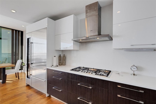 kitchen with light hardwood / wood-style flooring, stainless steel built in refrigerator, dark brown cabinetry, white cabinets, and wall chimney exhaust hood