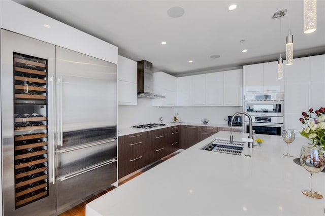 kitchen with sink, white cabinetry, hanging light fixtures, stainless steel appliances, and wall chimney exhaust hood