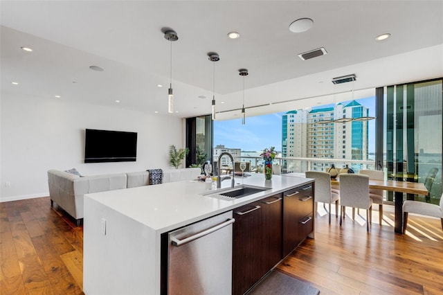 kitchen featuring sink, decorative light fixtures, dark brown cabinets, stainless steel dishwasher, and an island with sink