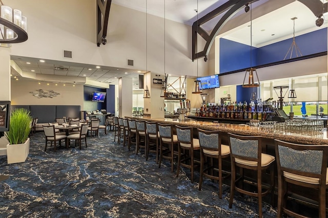 bar with decorative light fixtures, dark carpet, and a high ceiling