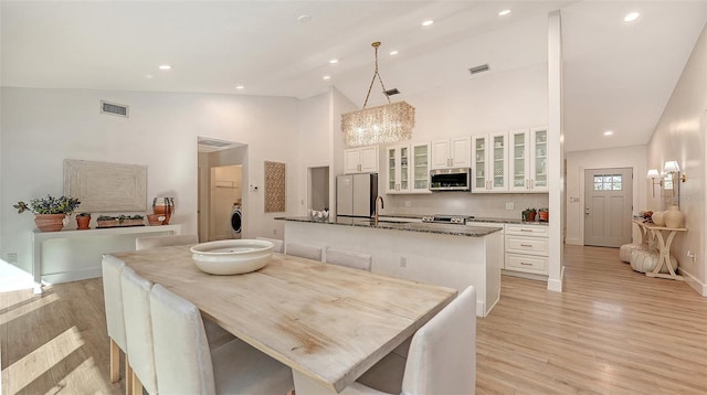 dining space with high vaulted ceiling, light hardwood / wood-style floors, sink, and washer / dryer