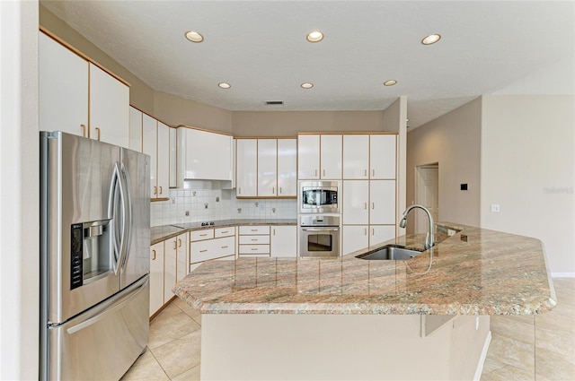 kitchen with sink, white cabinets, light stone counters, stainless steel appliances, and a center island with sink