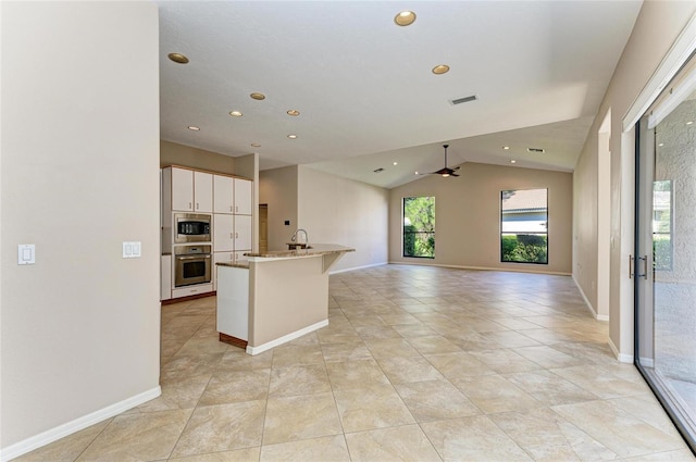 kitchen featuring sink, appliances with stainless steel finishes, light stone counters, white cabinets, and vaulted ceiling