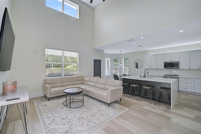 living room featuring light hardwood / wood-style floors, sink, a high ceiling, and a wealth of natural light