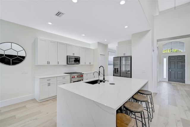 kitchen featuring stainless steel appliances, sink, white cabinets, and a kitchen island with sink