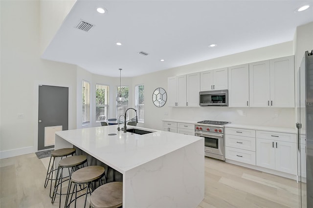 kitchen featuring appliances with stainless steel finishes, an island with sink, sink, white cabinets, and hanging light fixtures