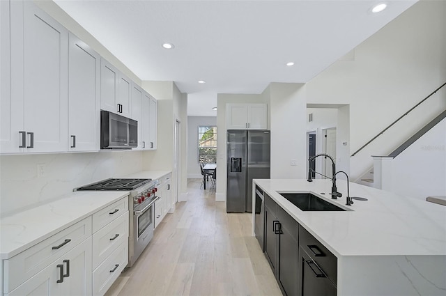 kitchen with sink, appliances with stainless steel finishes, white cabinetry, a kitchen island with sink, and light stone counters