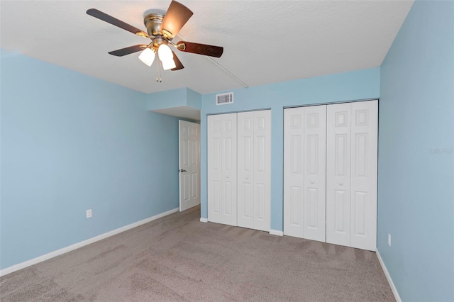 unfurnished bedroom featuring ceiling fan, a textured ceiling, multiple closets, and carpet