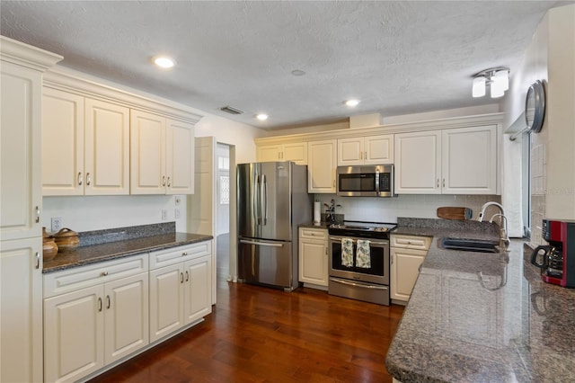 kitchen with sink, appliances with stainless steel finishes, backsplash, dark hardwood / wood-style flooring, and dark stone counters