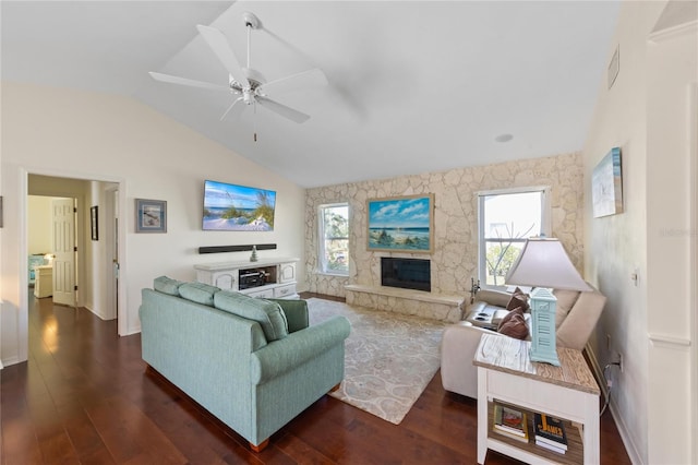 living room with lofted ceiling, dark hardwood / wood-style floors, a stone fireplace, and ceiling fan