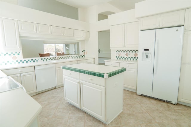 kitchen with tasteful backsplash, white appliances, a kitchen island, and white cabinets