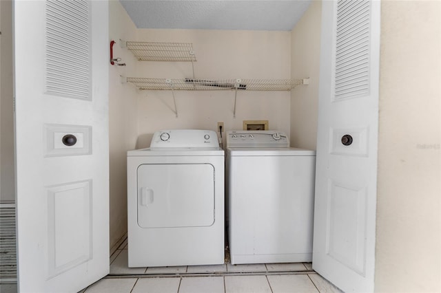 clothes washing area with light tile patterned floors, washer and clothes dryer, and a textured ceiling