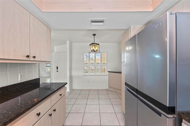 kitchen featuring pendant lighting, dark stone countertops, stainless steel fridge, and light brown cabinets