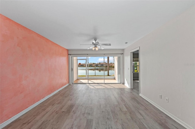 empty room featuring wood-type flooring, ceiling fan, and a water view