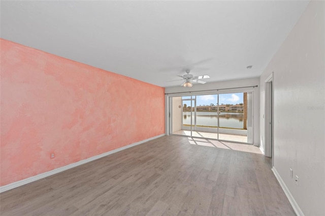 unfurnished living room featuring light hardwood / wood-style floors, ceiling fan, and a water view