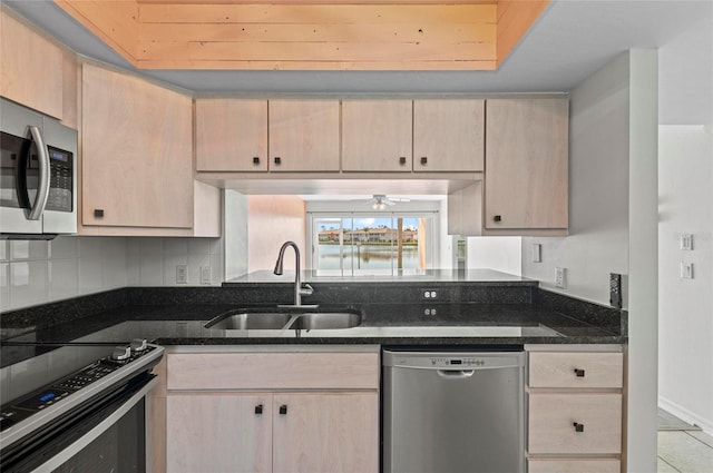 kitchen featuring stainless steel appliances, light brown cabinetry, sink, and dark stone counters