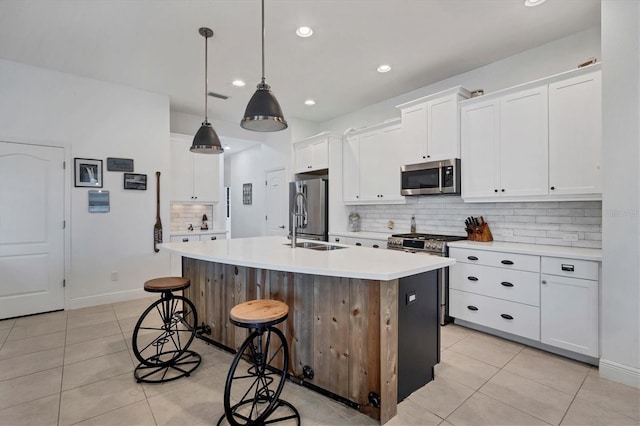 kitchen featuring light tile patterned floors, appliances with stainless steel finishes, an island with sink, pendant lighting, and white cabinets