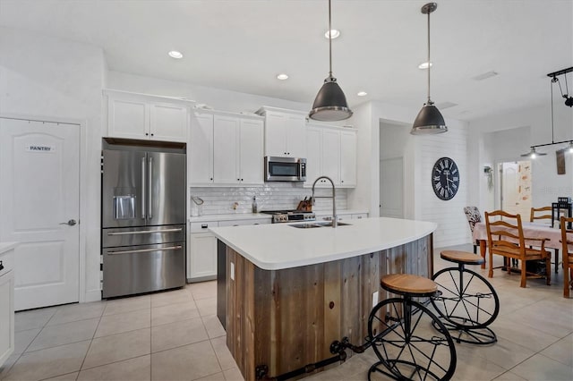 kitchen featuring pendant lighting, sink, appliances with stainless steel finishes, white cabinetry, and a center island with sink