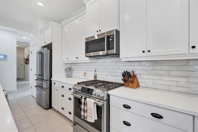 kitchen with stainless steel appliances, light tile patterned floors, white cabinets, and backsplash