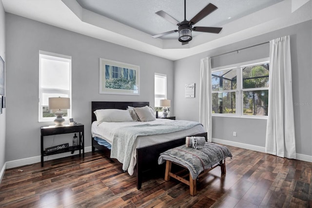 bedroom featuring dark hardwood / wood-style floors, a textured ceiling, ceiling fan, and a tray ceiling