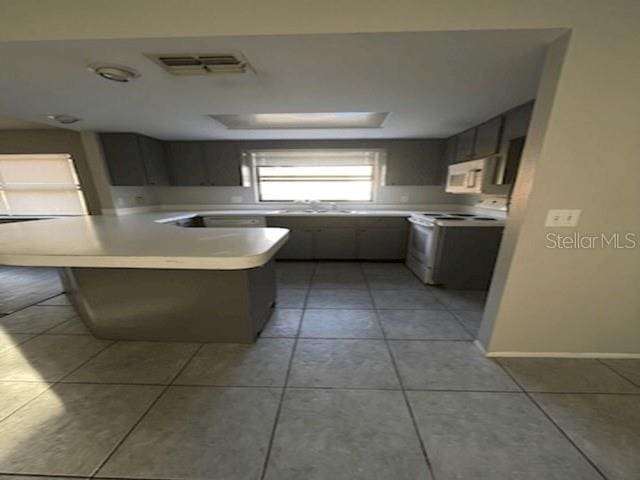 kitchen featuring light tile patterned flooring, kitchen peninsula, a kitchen bar, a tray ceiling, and white appliances