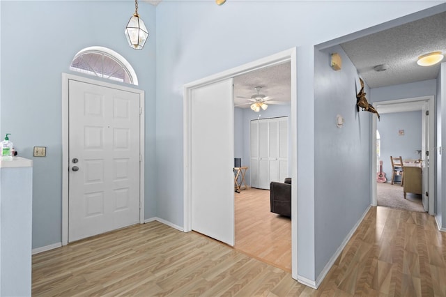 foyer entrance with ceiling fan, light hardwood / wood-style flooring, and a textured ceiling