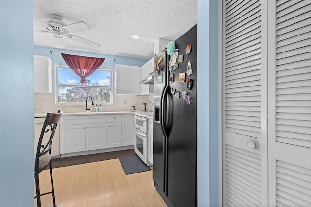 kitchen with sink, double oven range, white cabinets, black fridge with ice dispenser, and light wood-type flooring