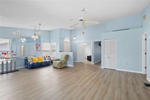 living area featuring baseboards, a ceiling fan, a textured ceiling, light wood-style floors, and high vaulted ceiling