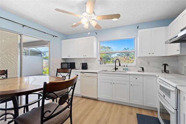 kitchen featuring white appliances, white cabinets, a sink, and light wood finished floors