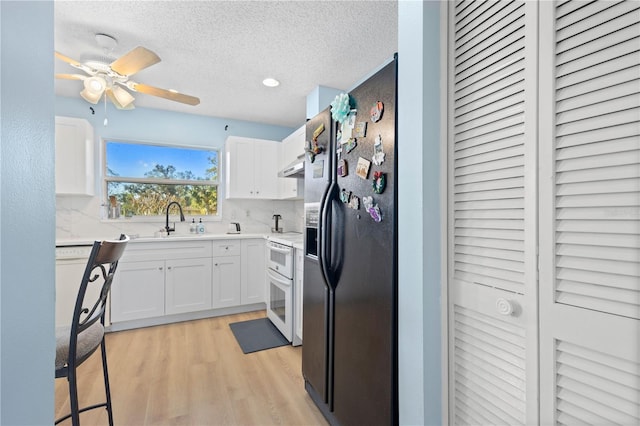 kitchen featuring light countertops, black fridge with ice dispenser, white cabinetry, a sink, and white range oven