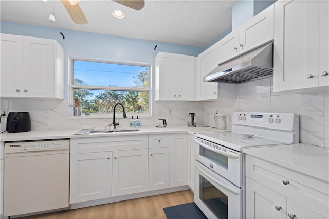 kitchen with white appliances, white cabinets, light countertops, under cabinet range hood, and a sink