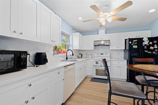 kitchen featuring light wood-style flooring, white cabinets, a sink, under cabinet range hood, and black appliances