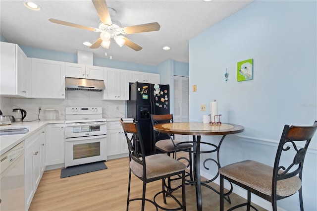 kitchen with under cabinet range hood, white appliances, white cabinets, backsplash, and light wood finished floors