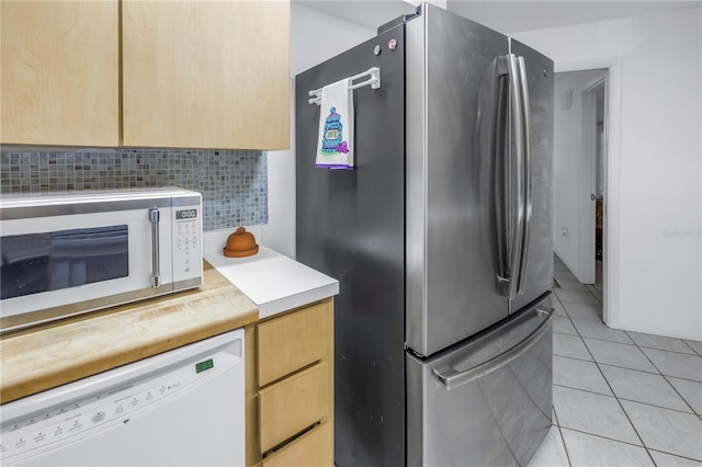 kitchen with light brown cabinetry, stainless steel refrigerator, tasteful backsplash, light tile patterned floors, and white dishwasher