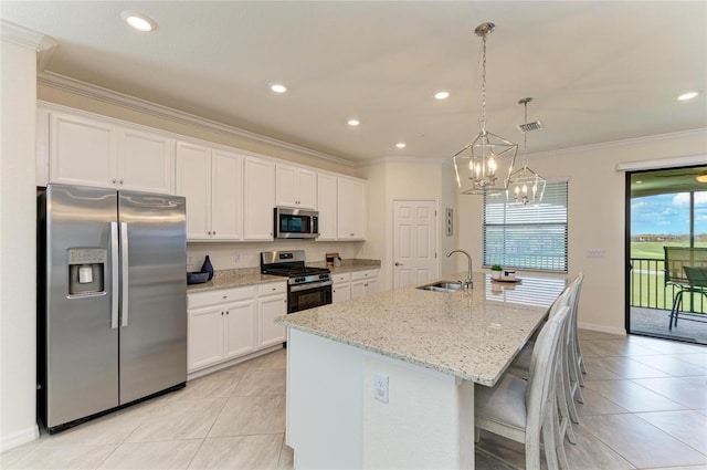 kitchen featuring appliances with stainless steel finishes, white cabinetry, light stone counters, a center island with sink, and decorative light fixtures