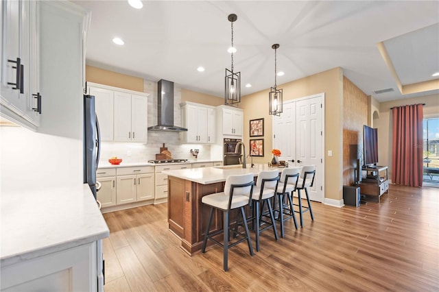 kitchen with stainless steel gas stovetop, white cabinetry, an island with sink, a kitchen bar, and wall chimney exhaust hood