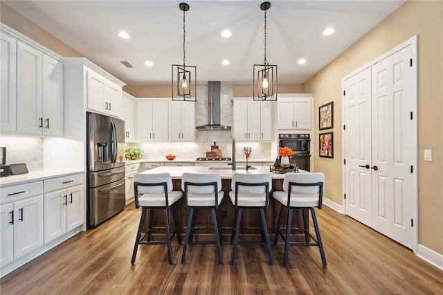 kitchen with stainless steel refrigerator with ice dispenser, wall chimney exhaust hood, an island with sink, and white cabinets