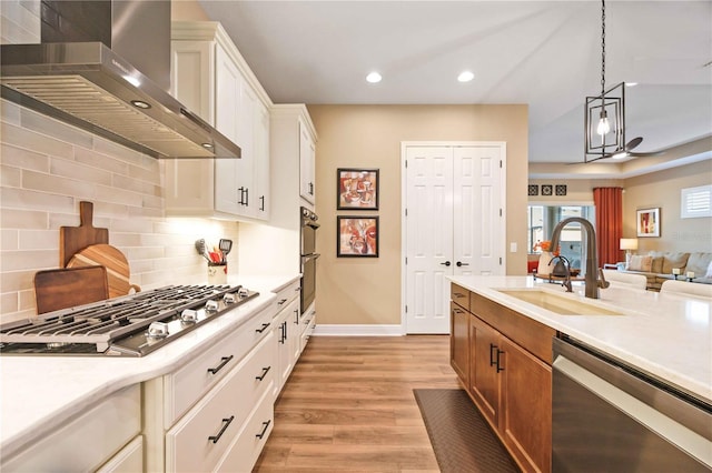 kitchen with decorative light fixtures, white cabinetry, sink, stainless steel appliances, and wall chimney exhaust hood