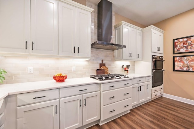 kitchen featuring black double oven, wall chimney exhaust hood, stainless steel gas cooktop, and white cabinets