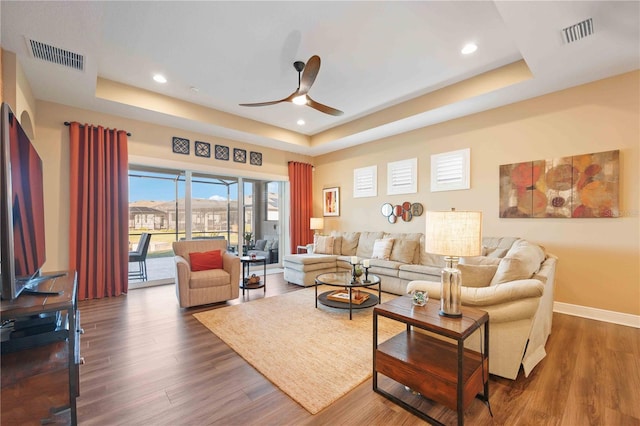 living room featuring ceiling fan, dark hardwood / wood-style flooring, and a tray ceiling