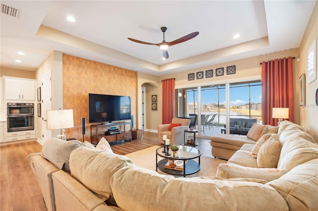 living room featuring light hardwood / wood-style flooring, ceiling fan, and a tray ceiling