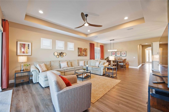 living room with hardwood / wood-style floors, a tray ceiling, and ceiling fan